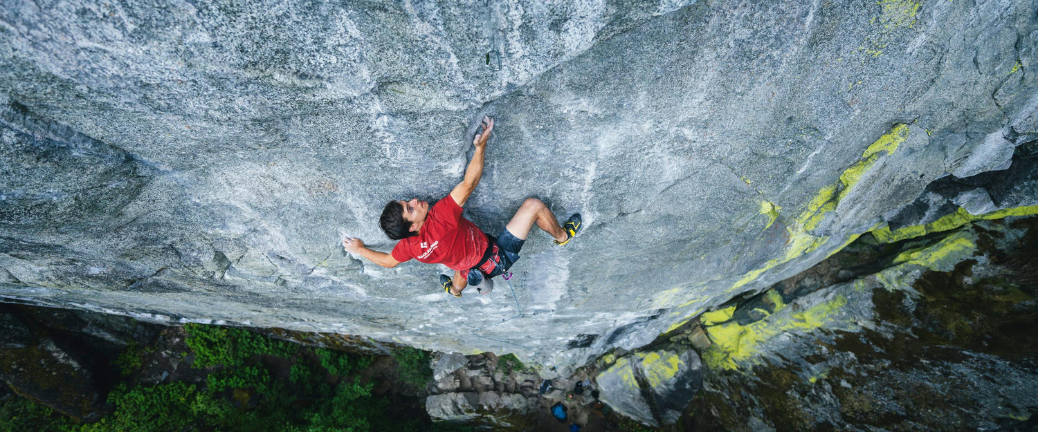 man in red t-shirt climbing a cliff face